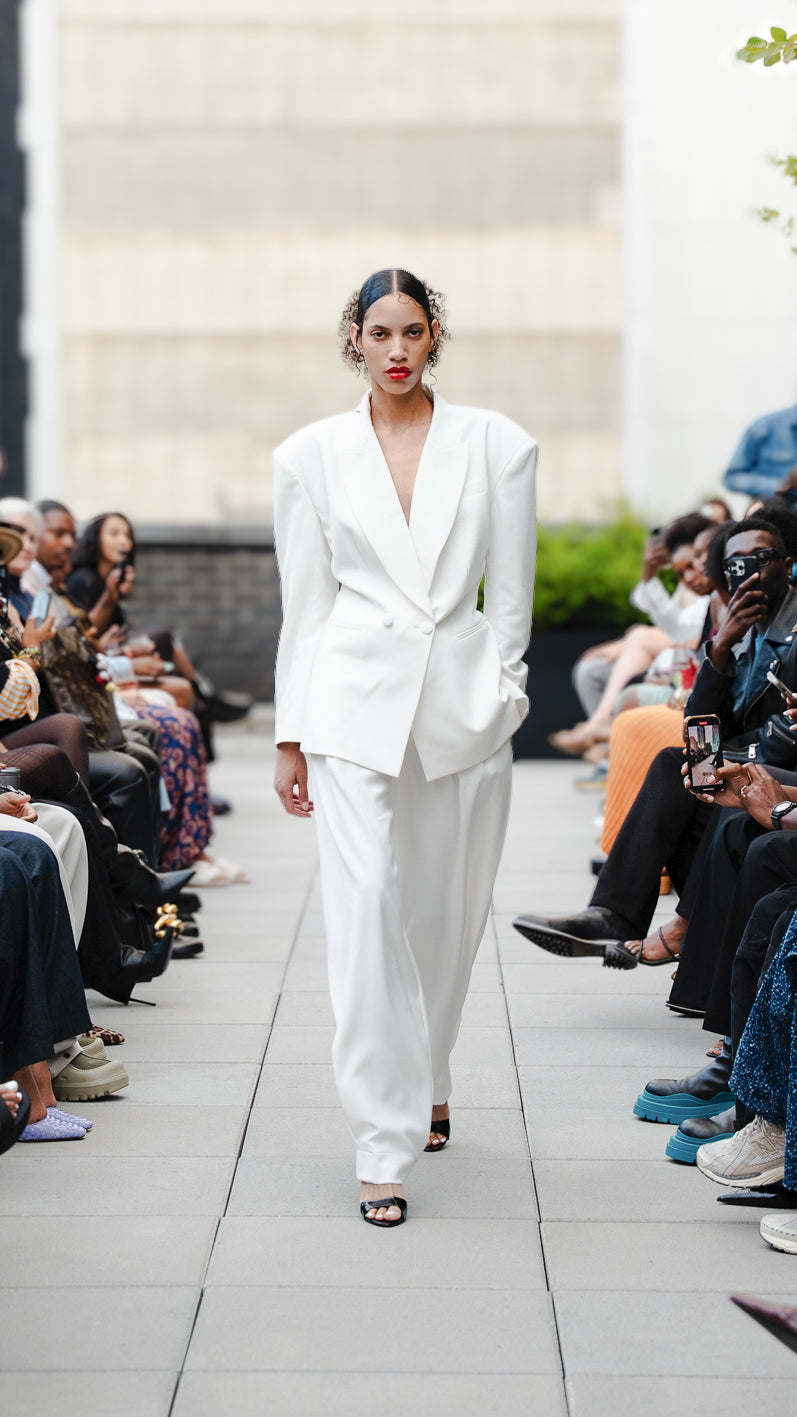 Ellie LeValle in a white suit set walking on Megan Renee's SS26 fashion show runway.