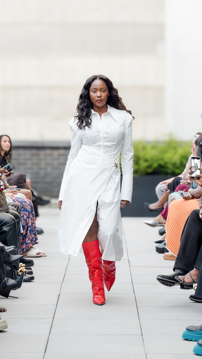 Kayelyn Salley walking on Megan Renee's SS26 fashion show runway wearing a white dress with red boots.