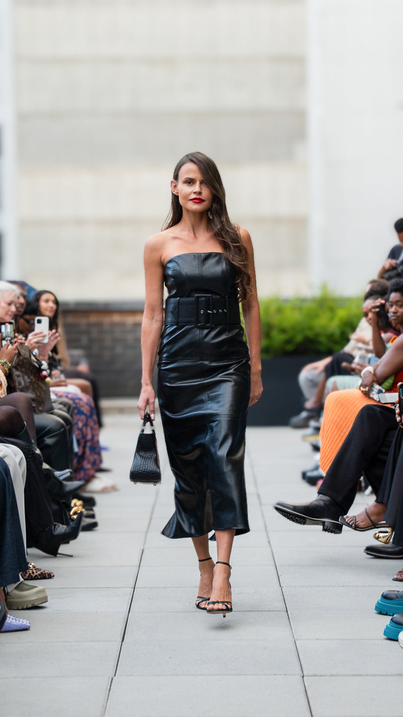 Olya Smith walking on Megan Renee's SS26 fashion show runway wearing a black vegan leather strapless dress.