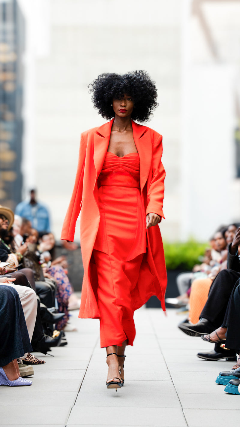 Kylar Smith in a red outfit walking on a fashion show runway for Megan Renee's SS26 collection.